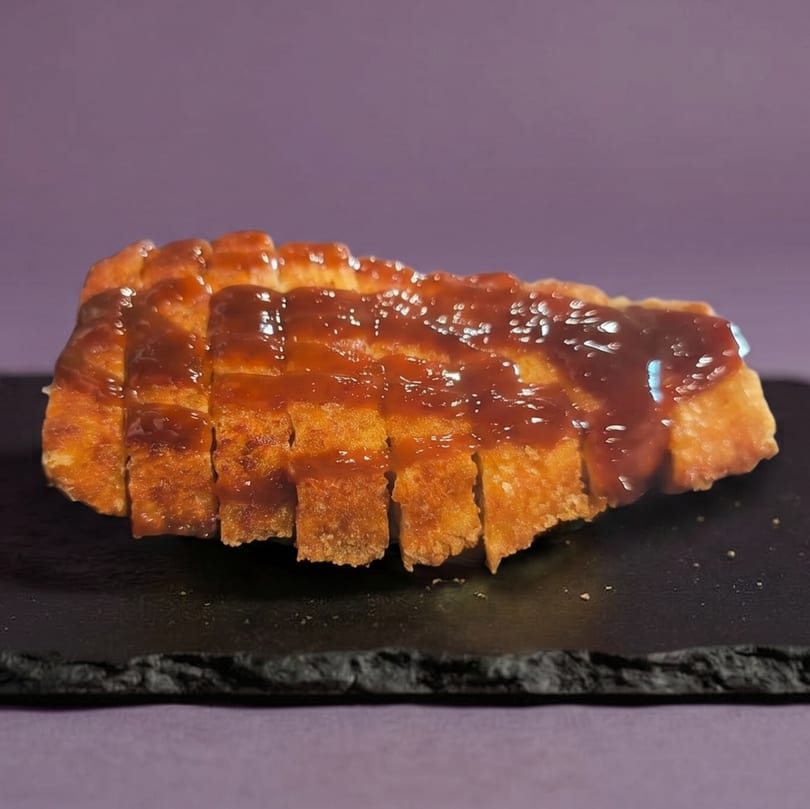 Crispy fried chicken cutlet, sliced into strips, drizzled with a glossy brown sauce on a dark plate.